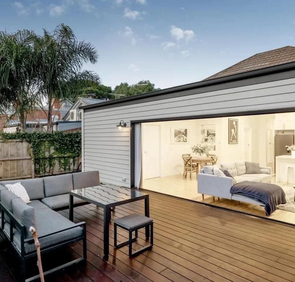Rear kitchen and living extension in pale weatherboard, with wide sliding doors opening onto a timber deck