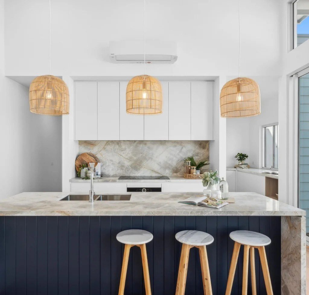 White kitchen with a navy timber-panelled island, stone benchtop and rattan pendant lights